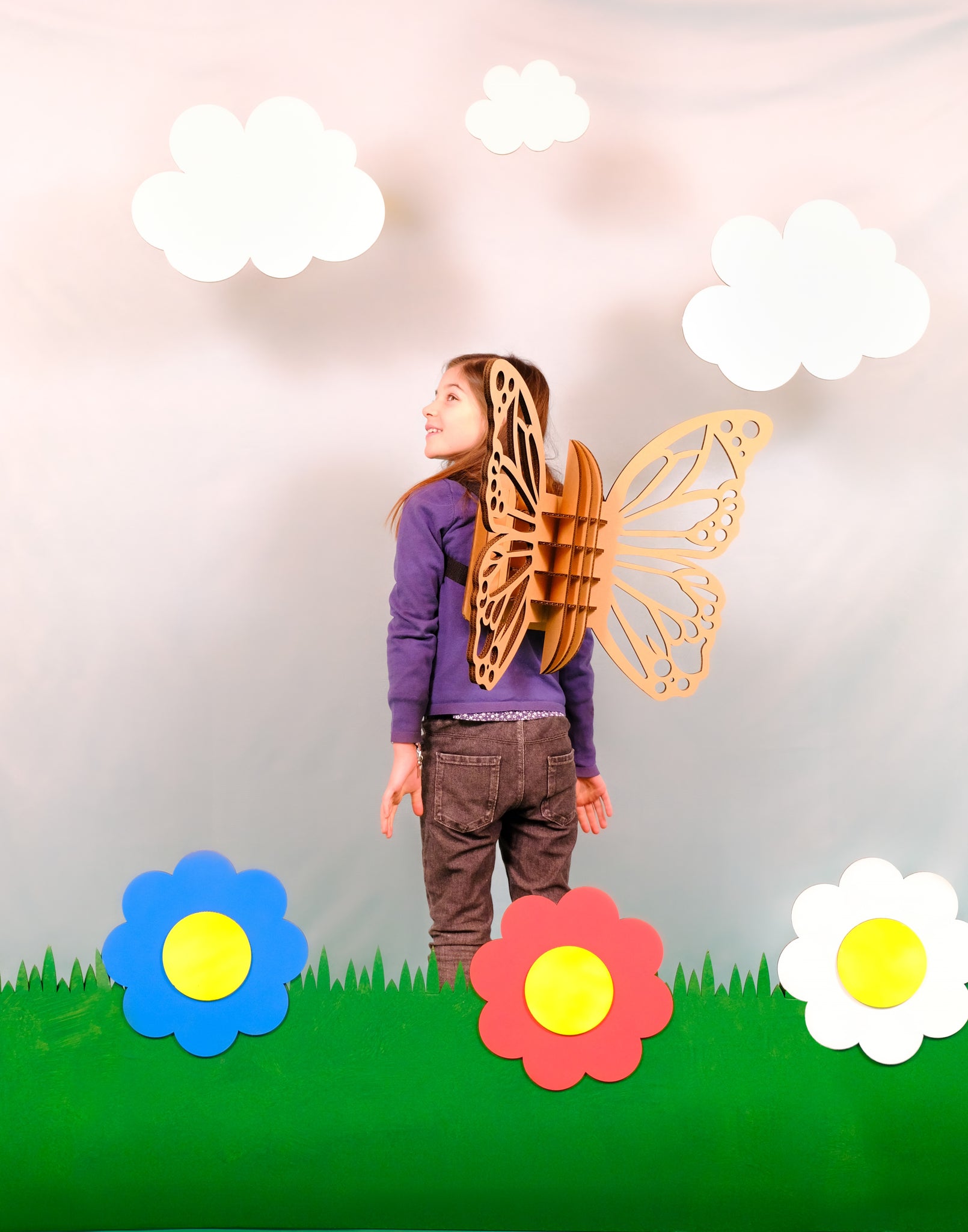 Un enfant avec un déguisement d'ailles de papillon en carton recyclé à assembler, décorer, colorier et peindre soi-même avec des fleurs en carton et des nuages en carton