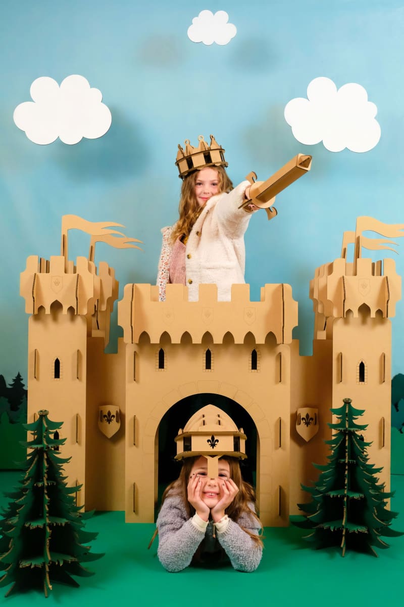 Deux enfants dans un château fort en carton recyclé et en déguisement de chevalier avec épée, bouclier, couronne et casque en carton recyclé à assembler, décorer, peindre et colorier soi-même avec nuage en carton et sapin en carton