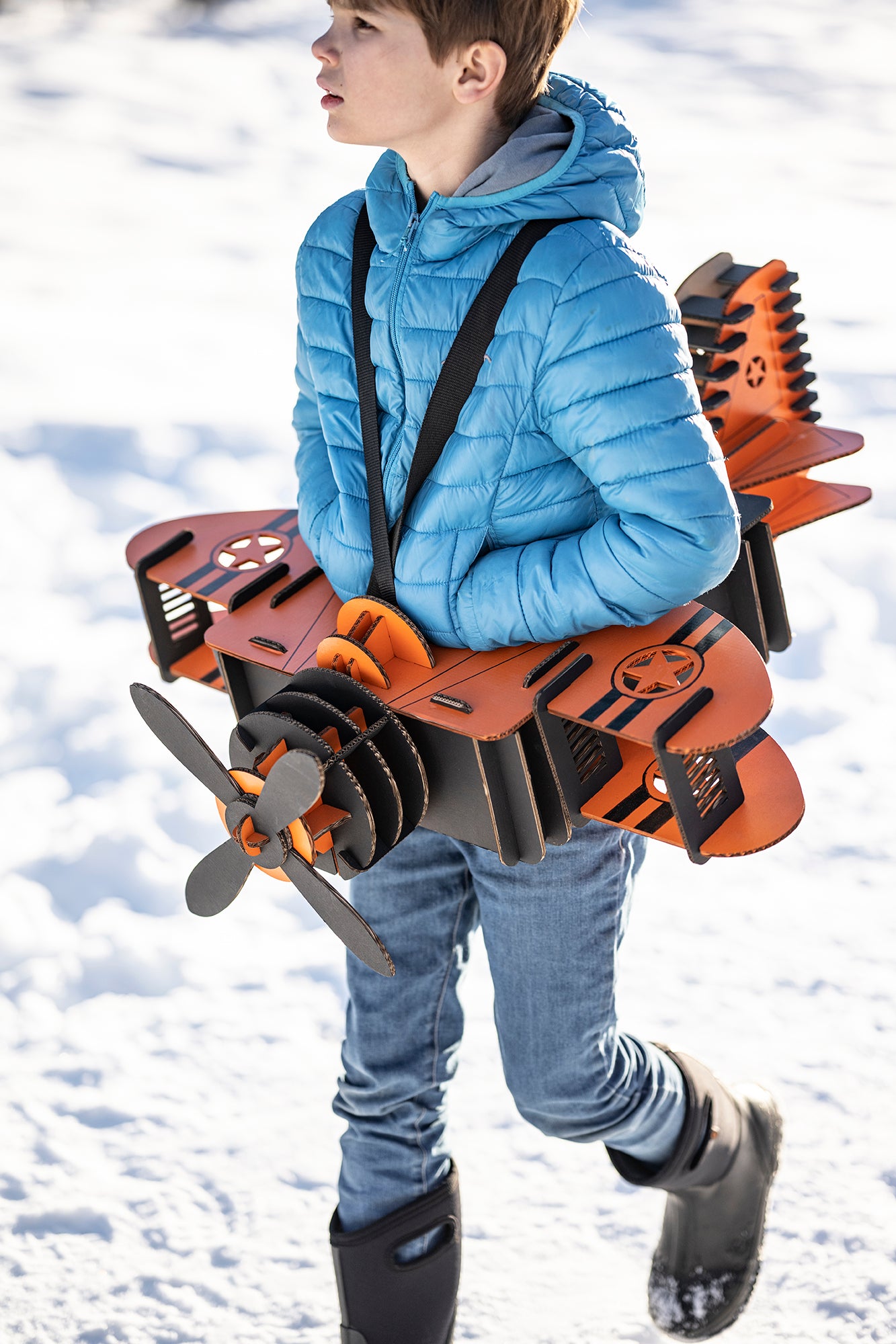 Un enfant en déguisement d'avion en carton recyclé orange et noir dans la neige