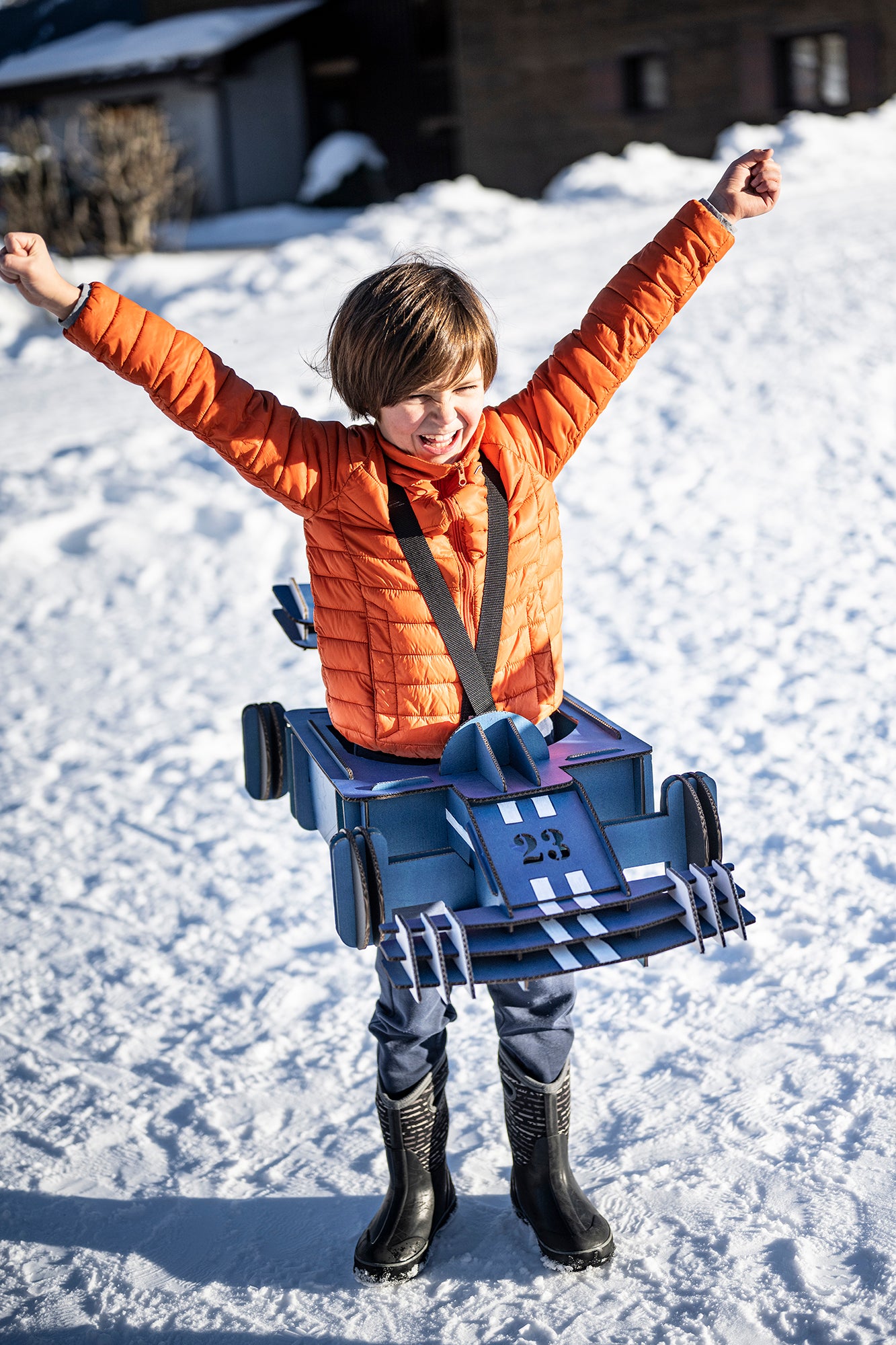 Un enfant avec un déguisement de formule 1 bleue en carton recyclé sur de la neige Tonton Carton