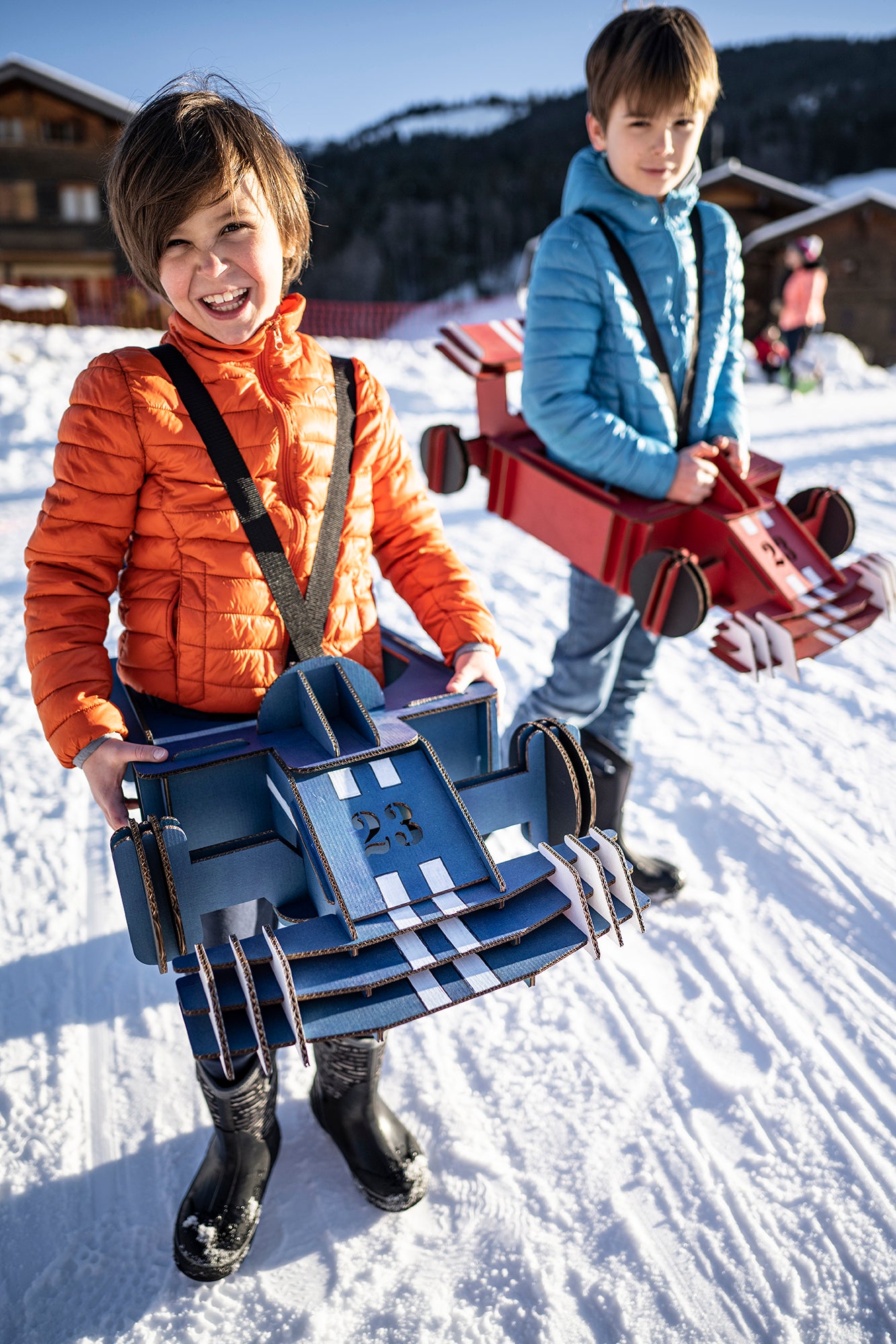Deux enfants avec des déguisements de formule 1 rouge et bleue en carton recyclé sur de la neige Tonton Carton