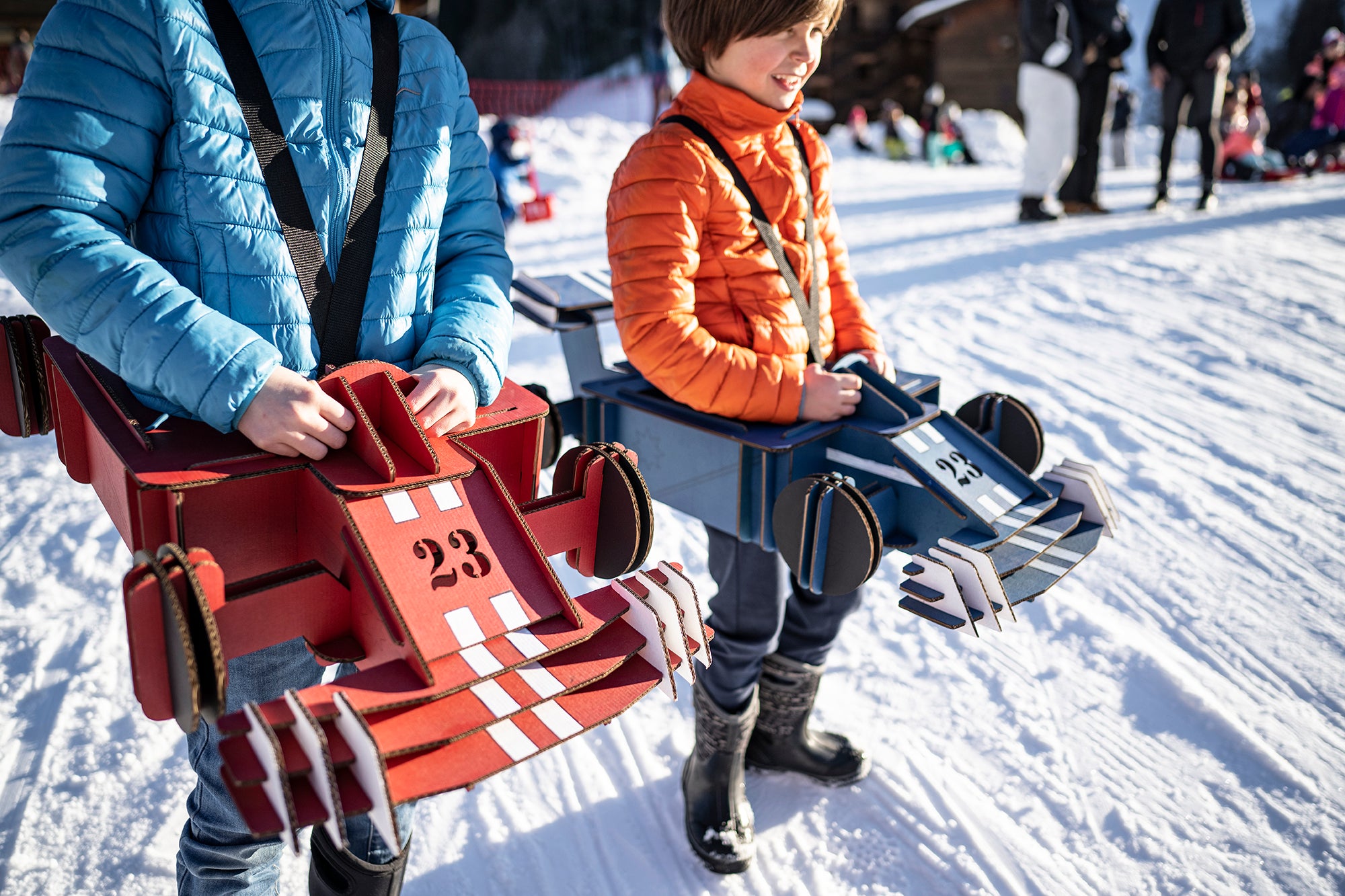 Deux enfants avec des déguisements de formule 1 rouge et bleue en carton recyclé sur de la neige Tonton Carton